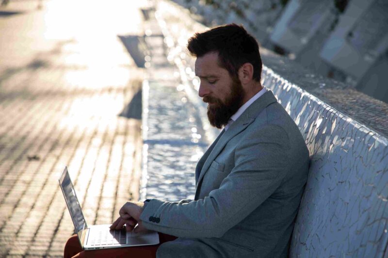 Well-dressed man working on a laptop outdoors beside a modern water feature, representing business, wealth, and luxury growth in the Sun Belt