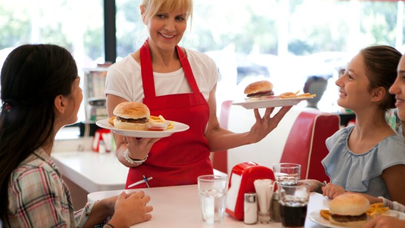 Waitress serves fast-food orders with burgers and fries to guests at a diner
