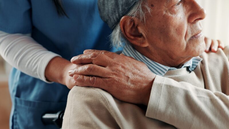 Caregiver comforting an older man in a wheelchair